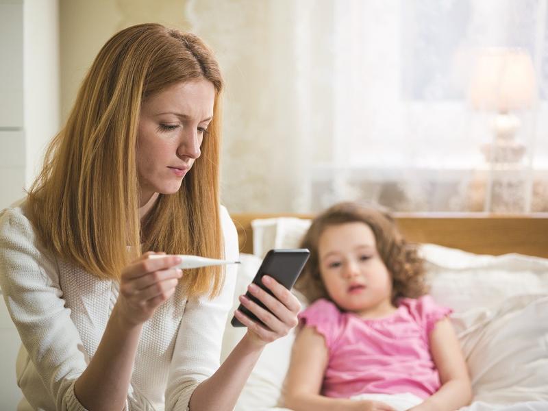 mom with sick daughter using her phone to call doctor