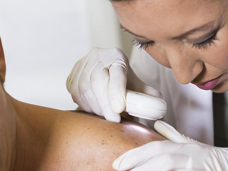 Patient leans forward as doctor examines skin of upper shoulder