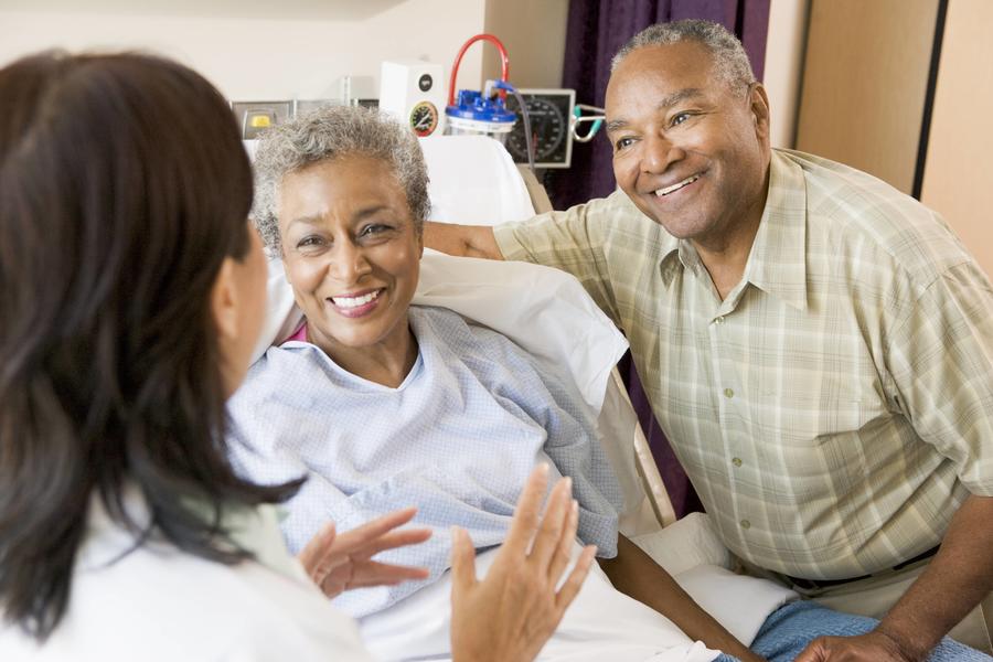 Patient in hospital bed smiling with doctor and spouse